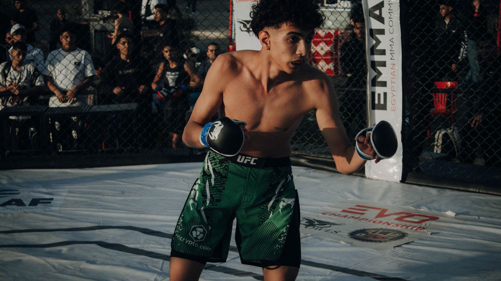 A young MMA fighter holding a balanced stance inside a competition cage