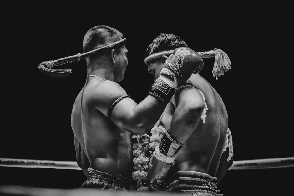 Two Muay Thai fighters engaged in the plum clinch position inside a ring