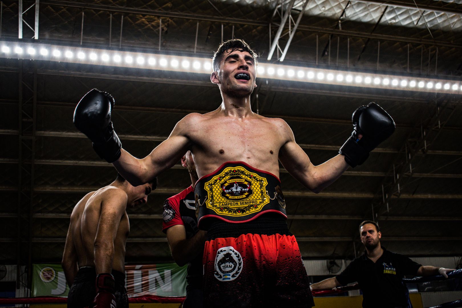 A triumphant champion with championship belt raises his arms in victory.