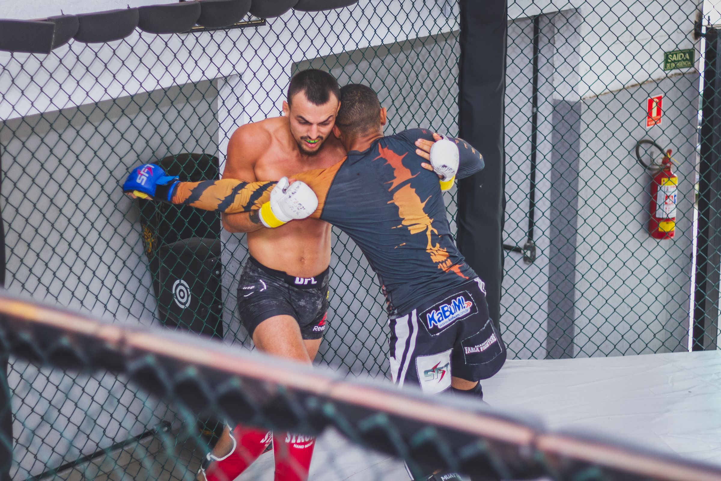 Two MMA fighters grappling against the cage