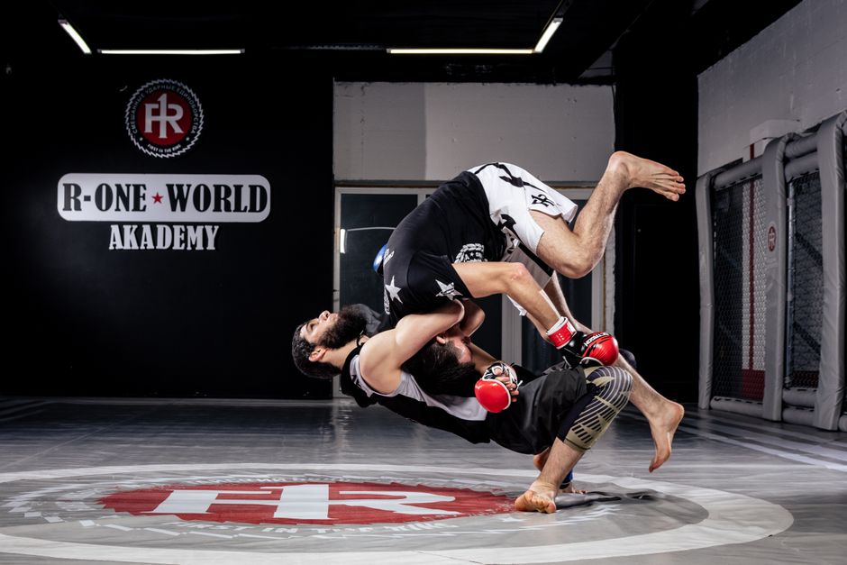 Two mixed martial artists during a dynamic takedown inside a training cage