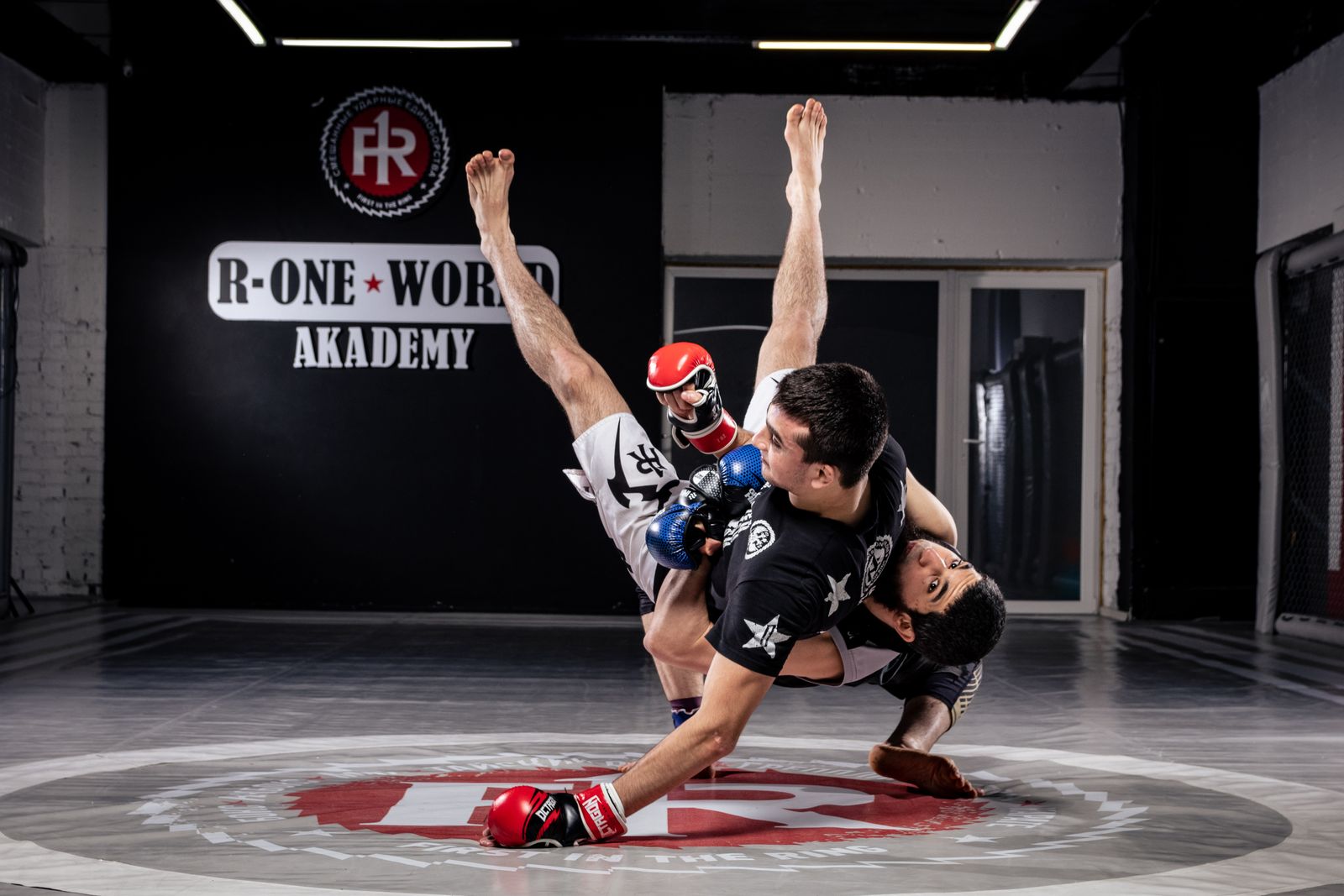 Two fighters in a takedown scramble in an MMA gym