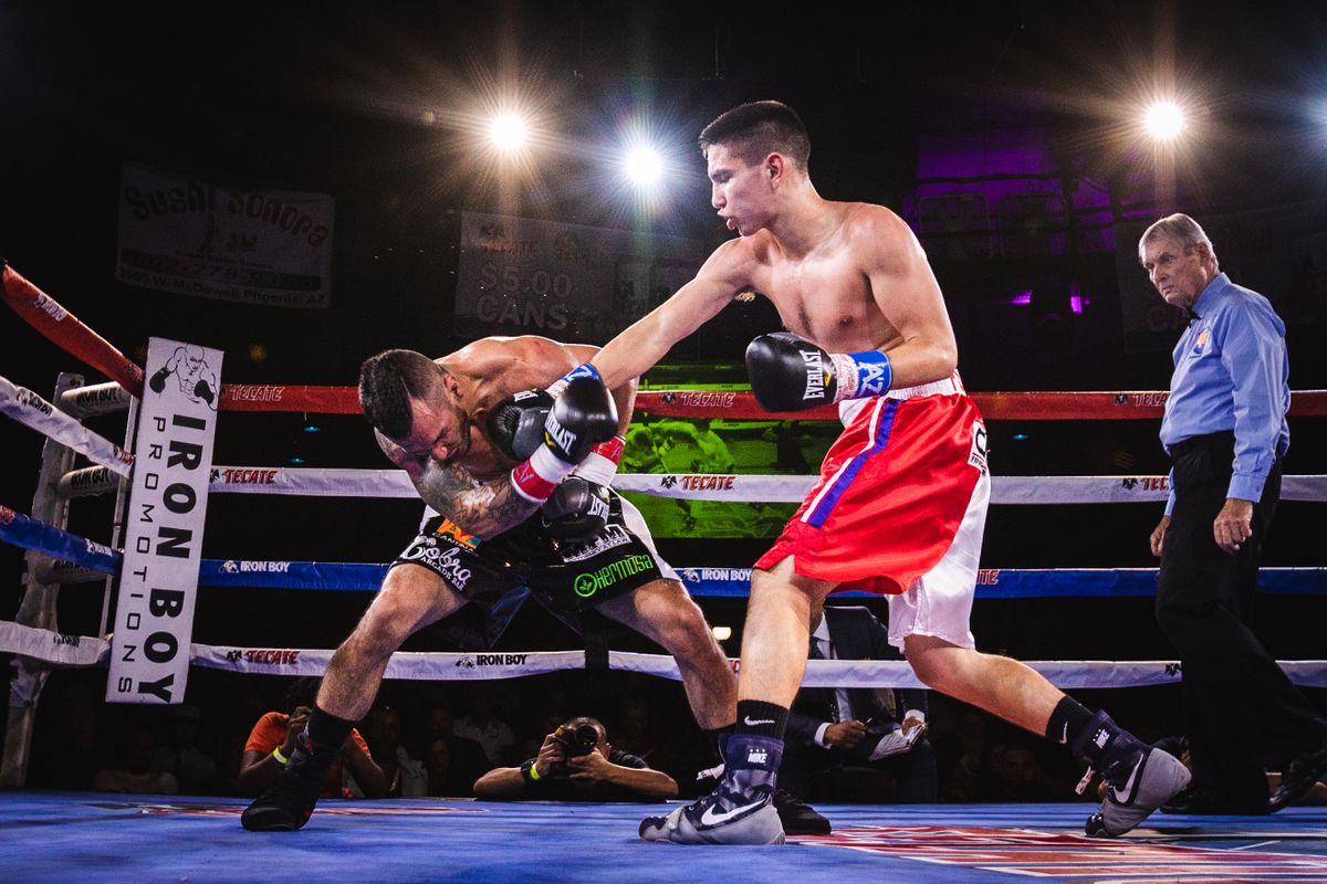 Professional boxing match under arena lights with a referee overseeing the action
