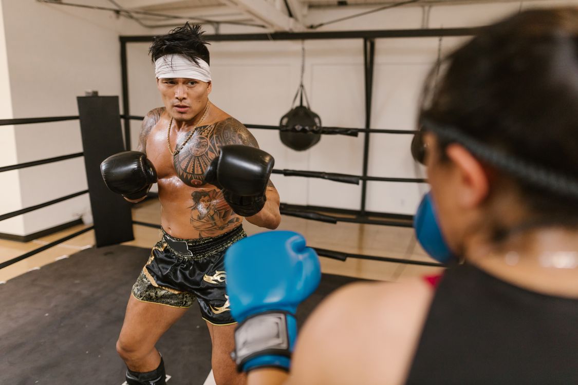Tattooed boxer with black gloves training in a gym ring